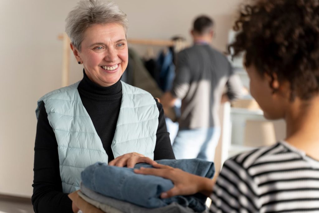 Femme souriante recevant une pile de vêtements pliés d'une aide à domicile